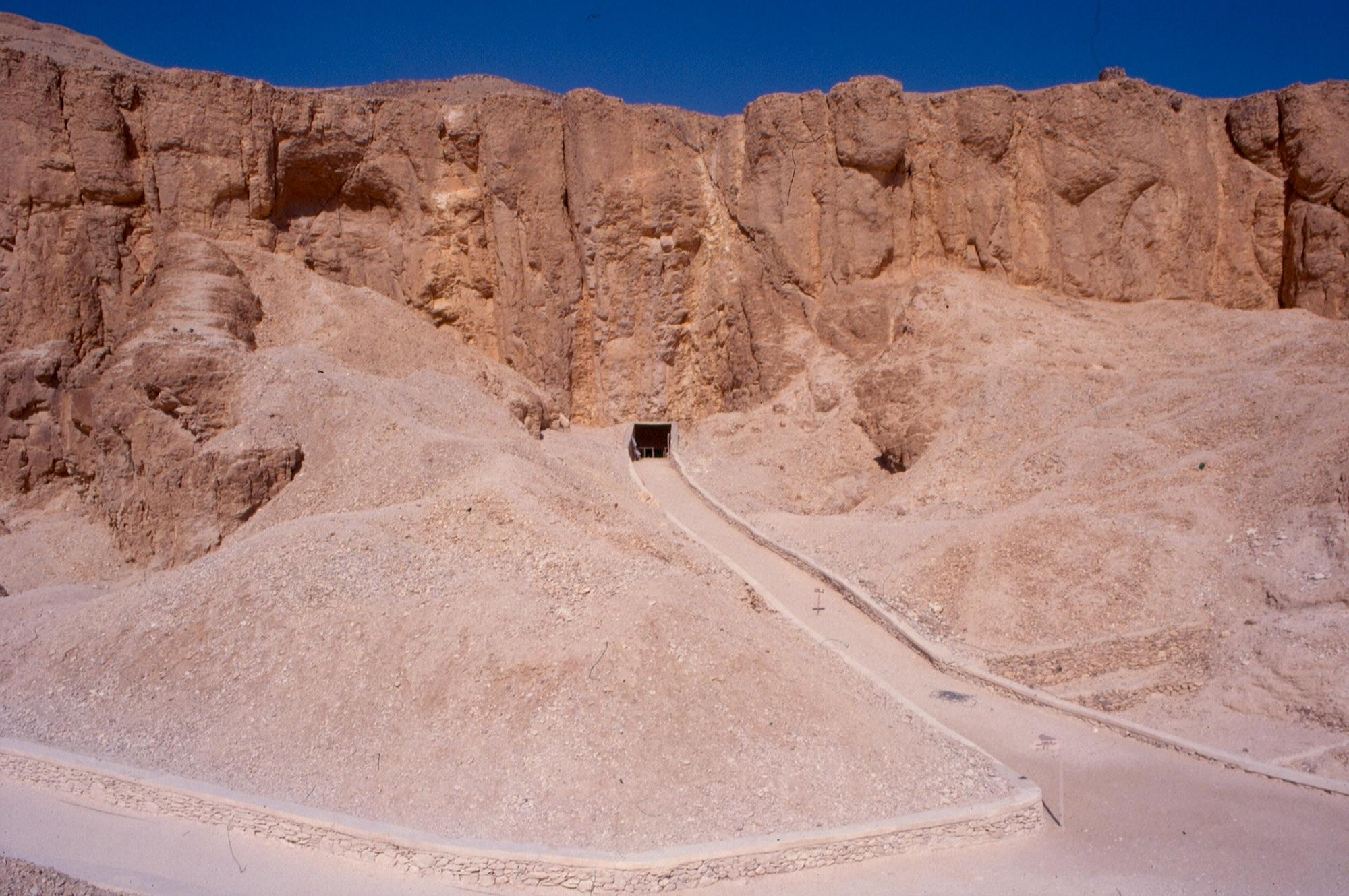 Tomb entrance at base of cliff with approach path.
